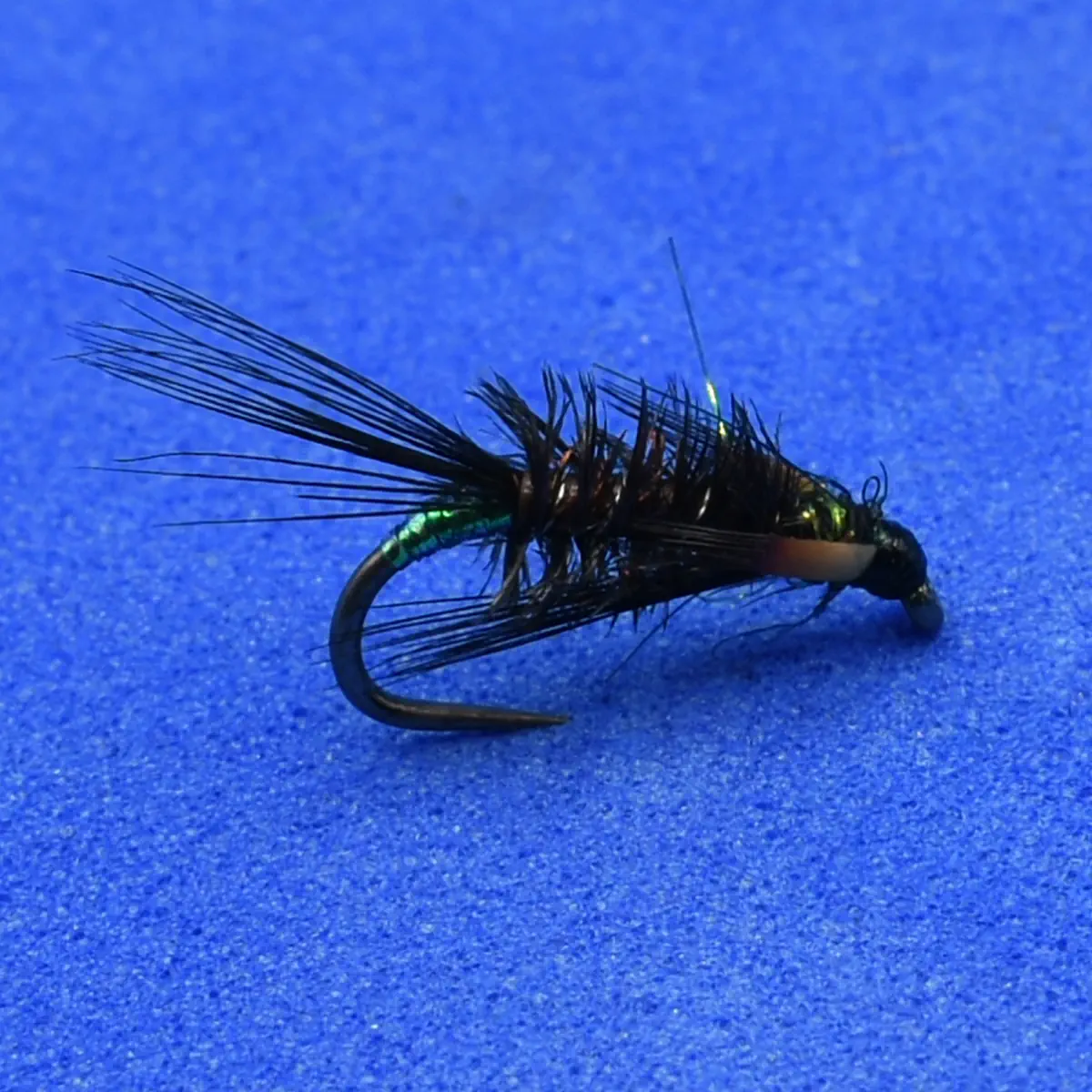 Close-up of a metallic green and black fishing fly with feathered hackle on a blue surface (artificial lure).