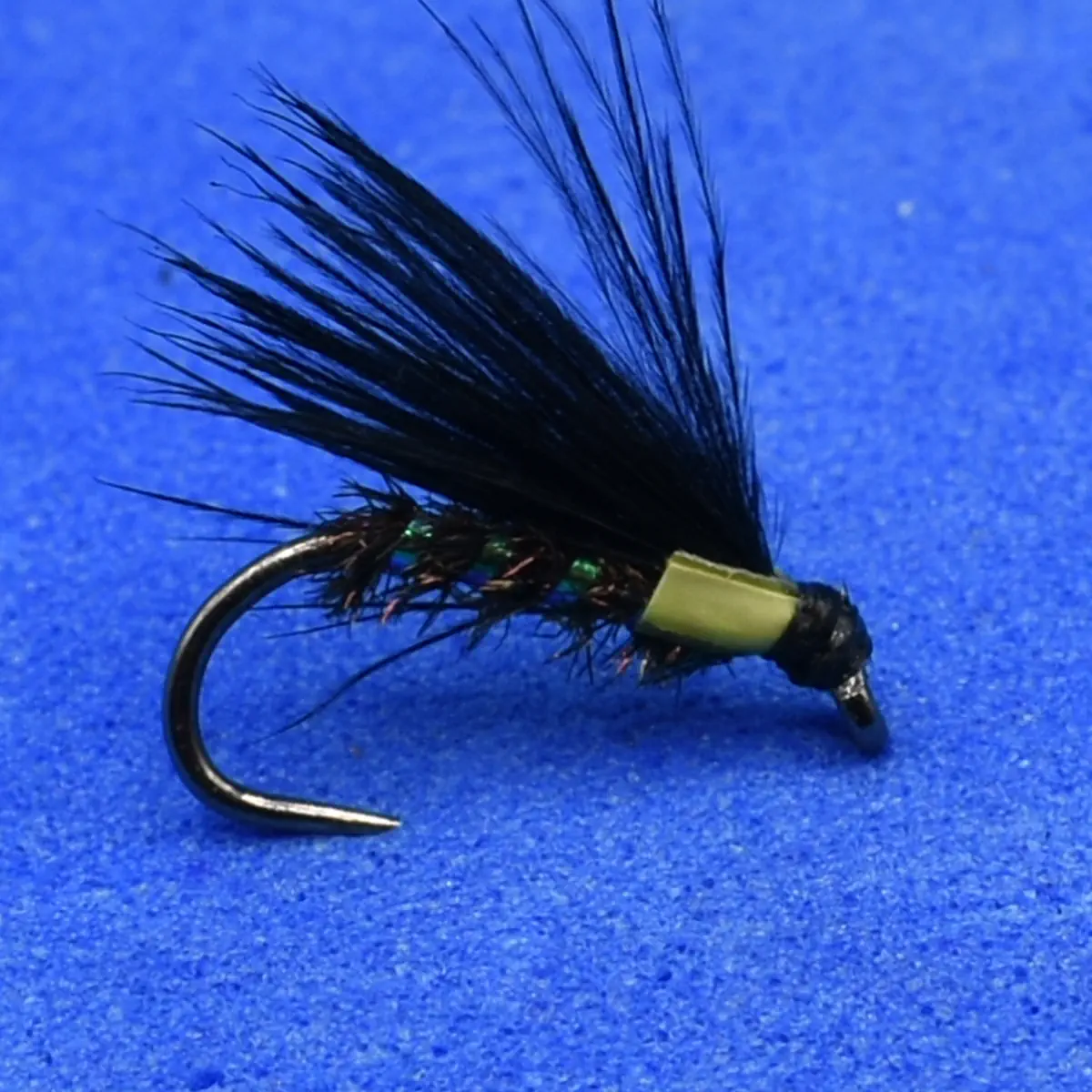 Black dry-fly fishing lure with a feathered hackle and green ribbed body on a curved hook used for fly fishing.