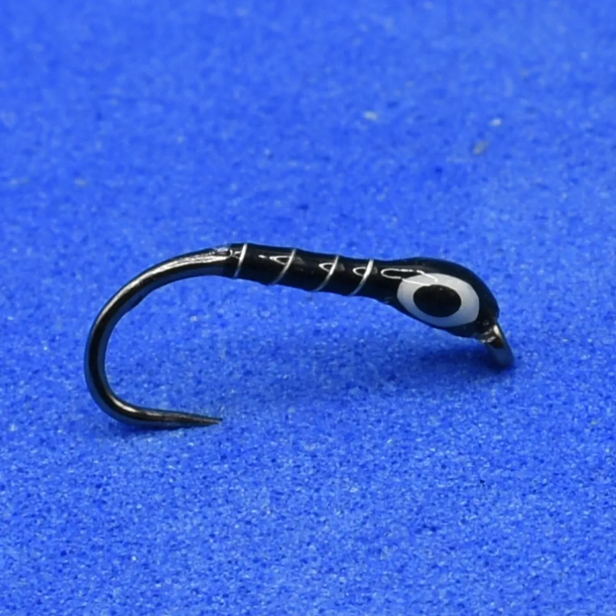 Close-up of a black curved fishing hook with white thread wrapping on a blue surface.