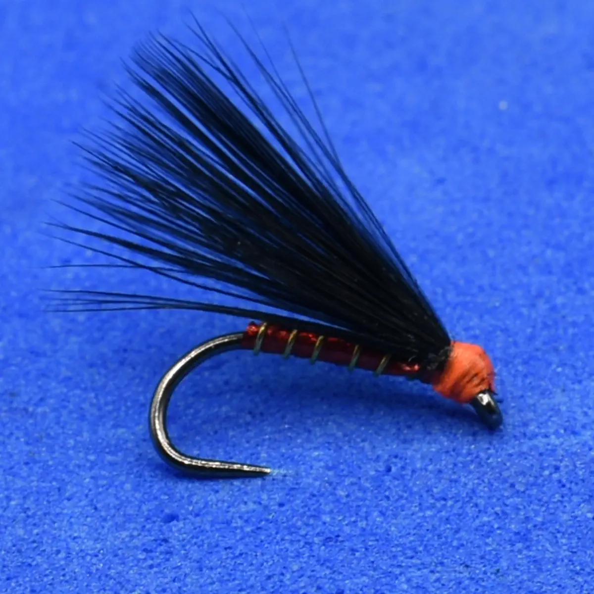 Close-up of a fishing fly lure with black feather tail, red-wrapped body, and a curved silver hook