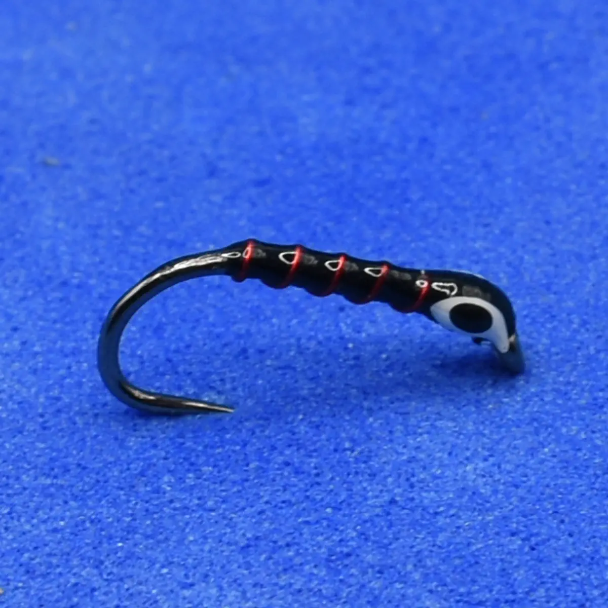 Close-up of a black fishing hook with red thread wraps on a blue background.