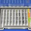 Open fly box with rows of colorful fishing flies arranged by size; bright feather lures on the right.