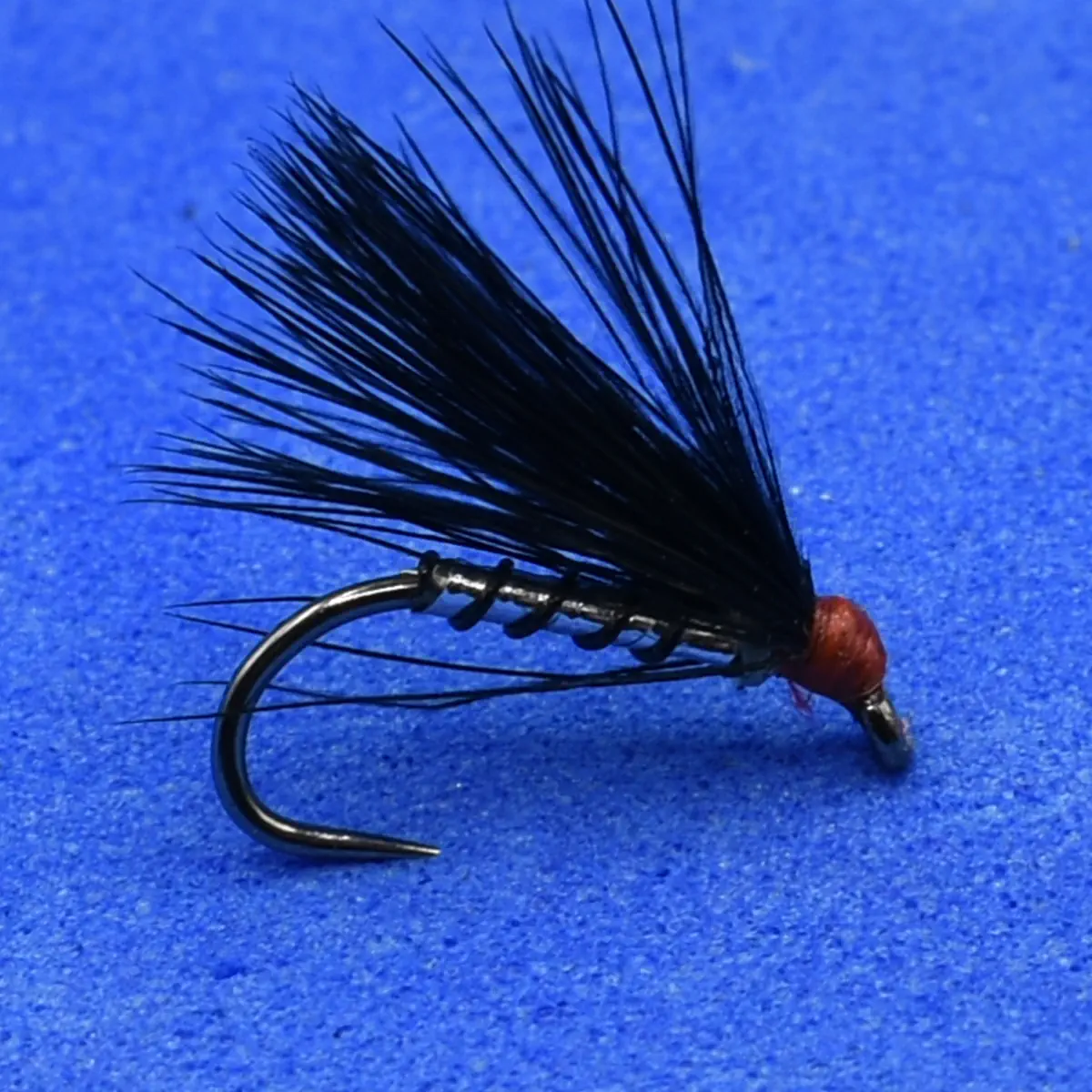 Black feathered fishing fly with a red bead head mounted on a curved hook, set against a blue background (trout fishing lure).