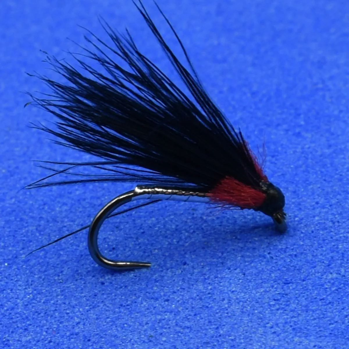 Fly fishing lure with black feather hackle and red body on a curved hook