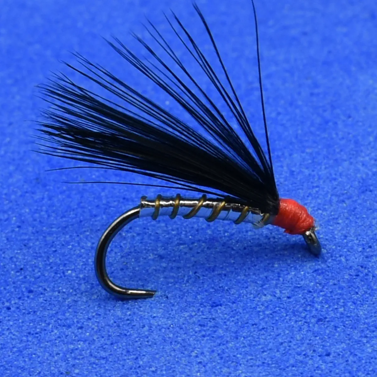 Artificial fishing fly: black hackle tail tied to a hook with red head, used as bait for fly fishing