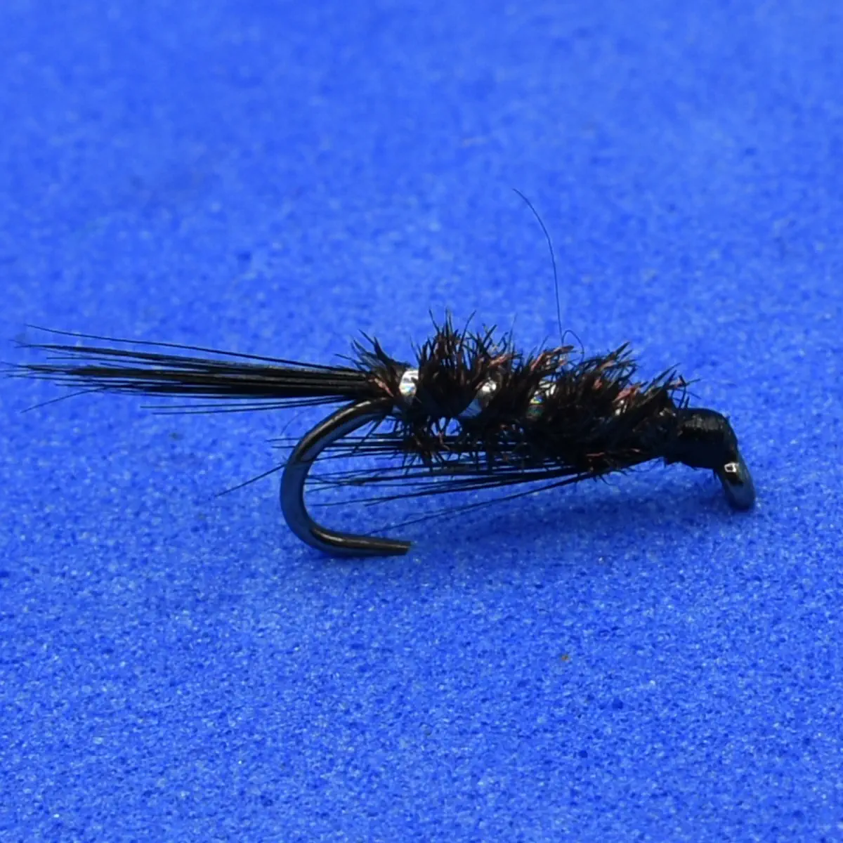 A black artificial fly lure for fly fishing with feathered hackle and a curved hook on a blue background.