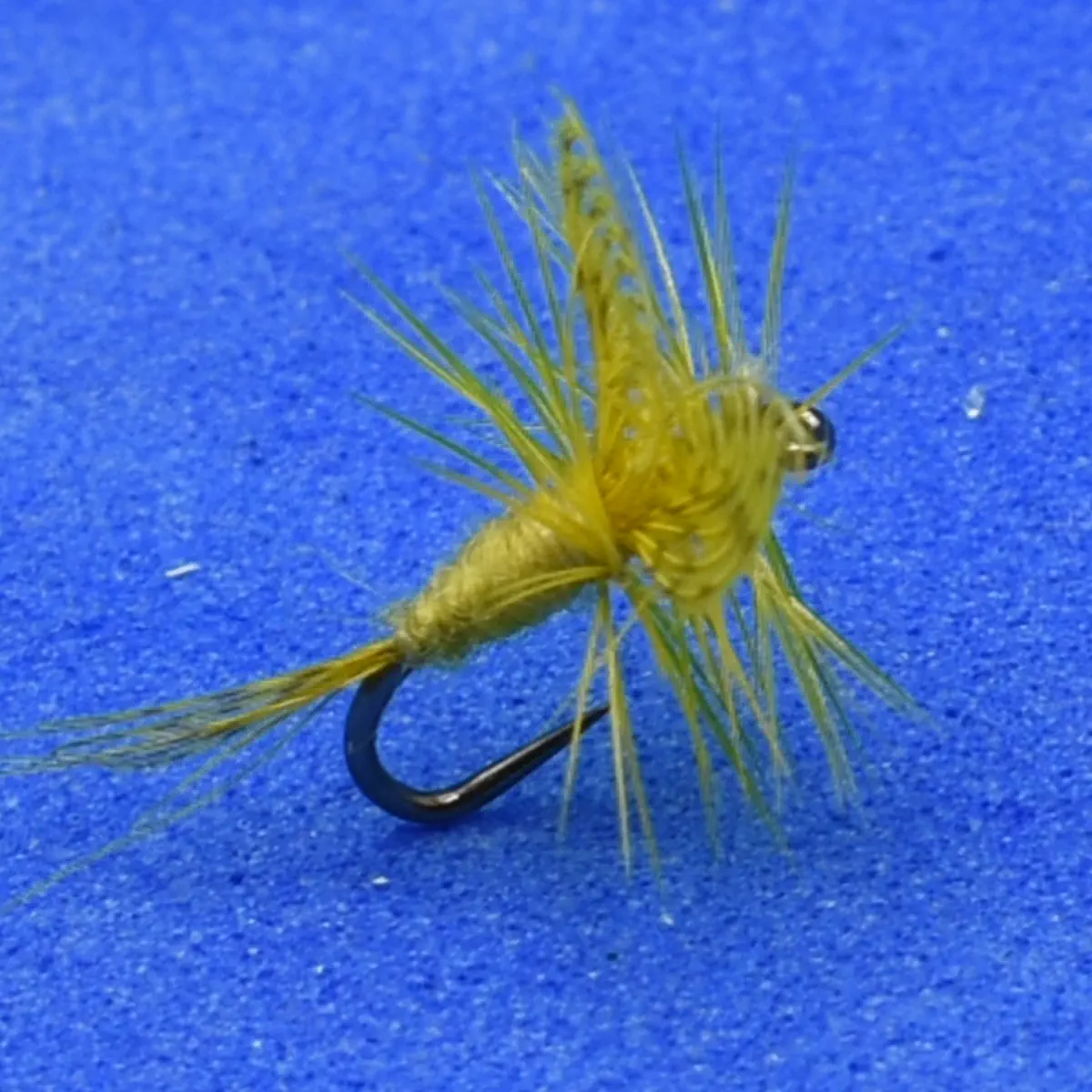 Yellow dry-fly fishing lure with feathered hackle on a curved hook, set against a blue background.