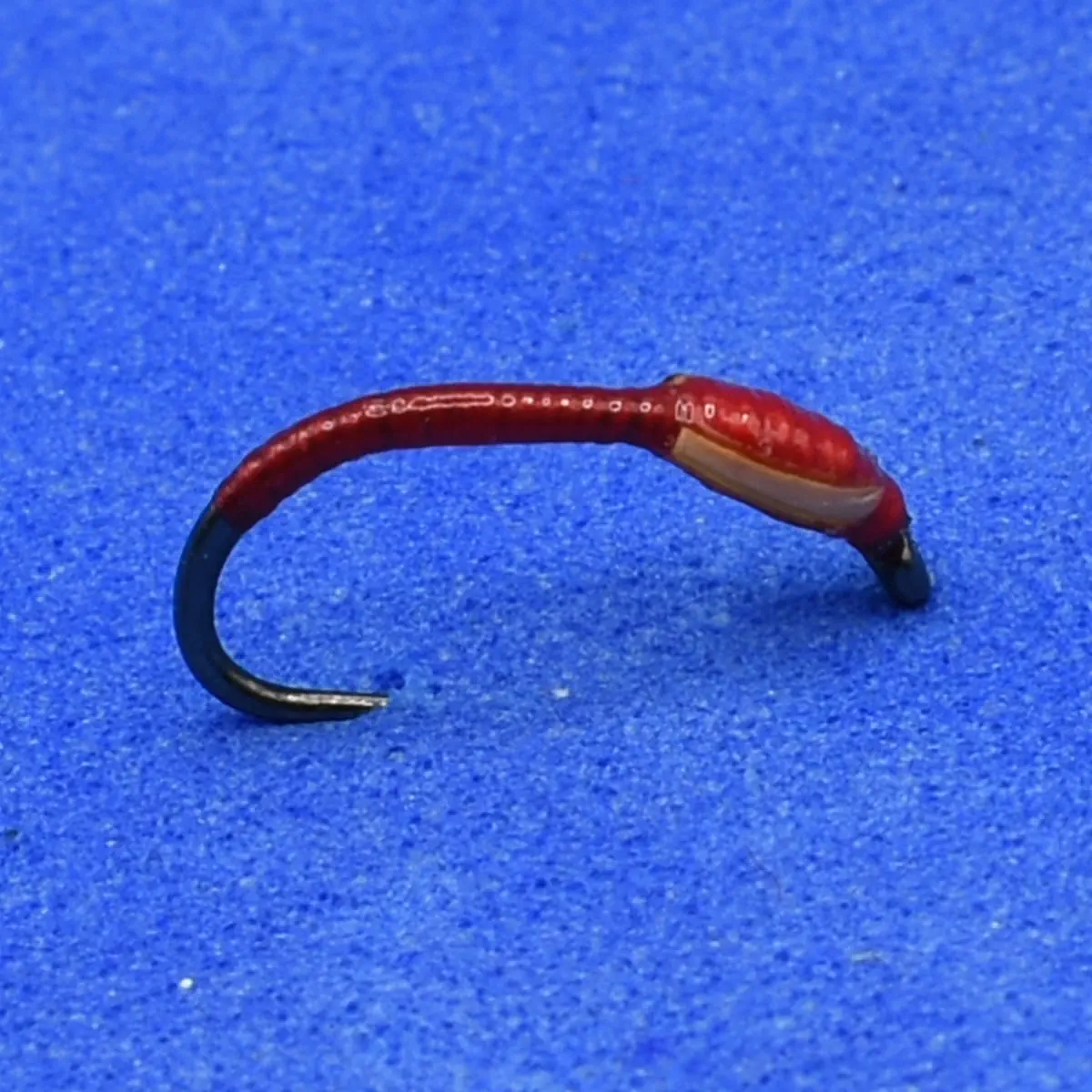 Red soft-plastic fishing lure shaped like a curved worm with a black hook end on a blue background
