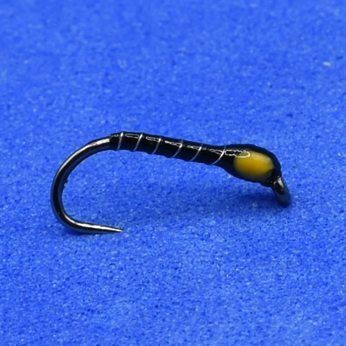 Close-up of a black fishing hook wrapped with white thread and a yellow bead on a blue background, a simple lure.