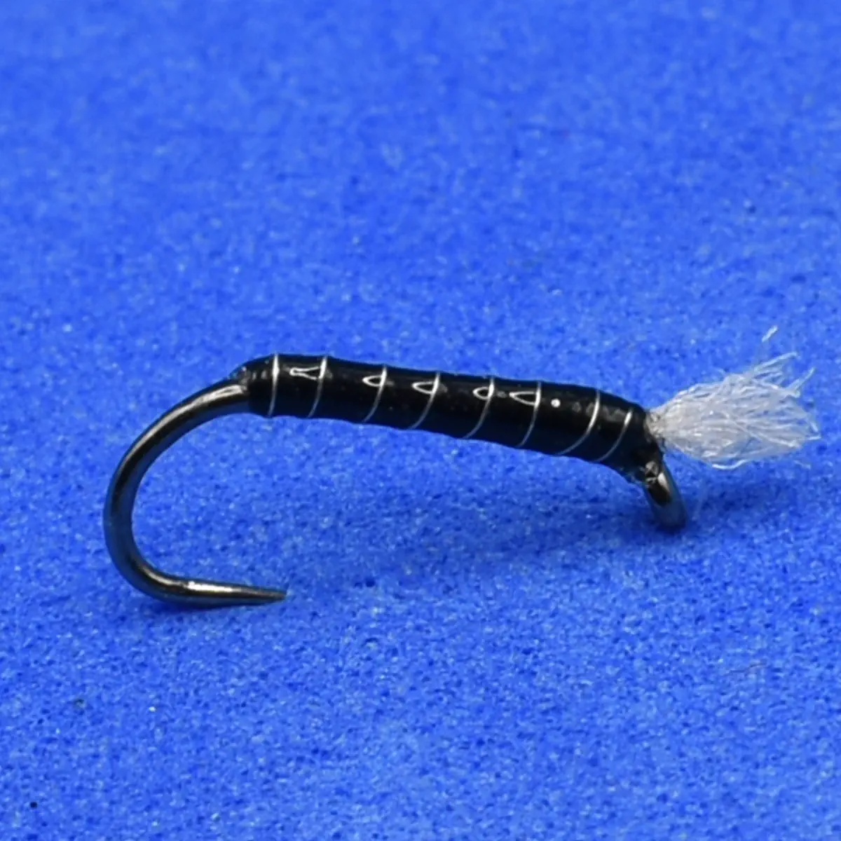 Black fly fishing lure with white thread wraps and a wispy tail on a blue background.