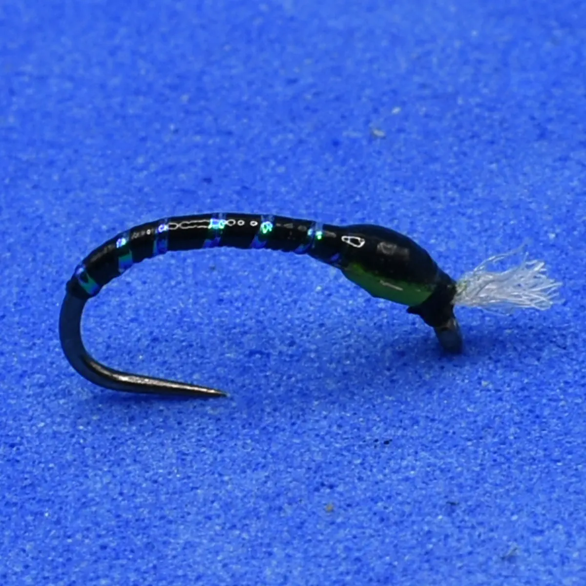 Black bead-head fly fishing lure with segmented body and white-tipped tail on blue background
