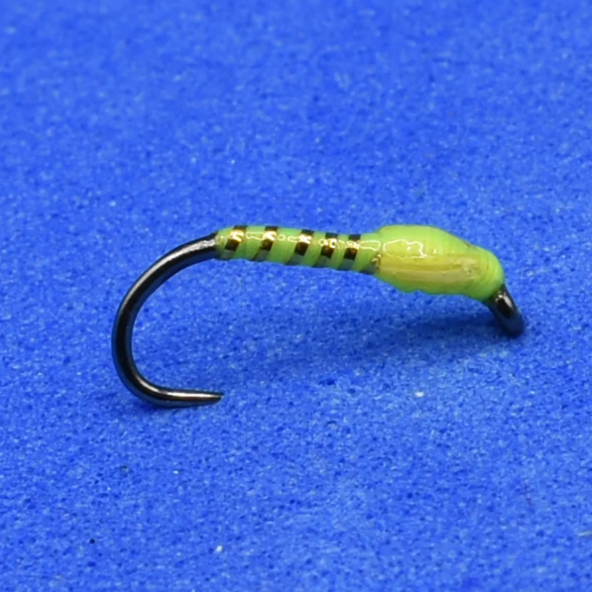 Green segmented soft plastic fishing lure on a curved black hook, with a translucent green head portion