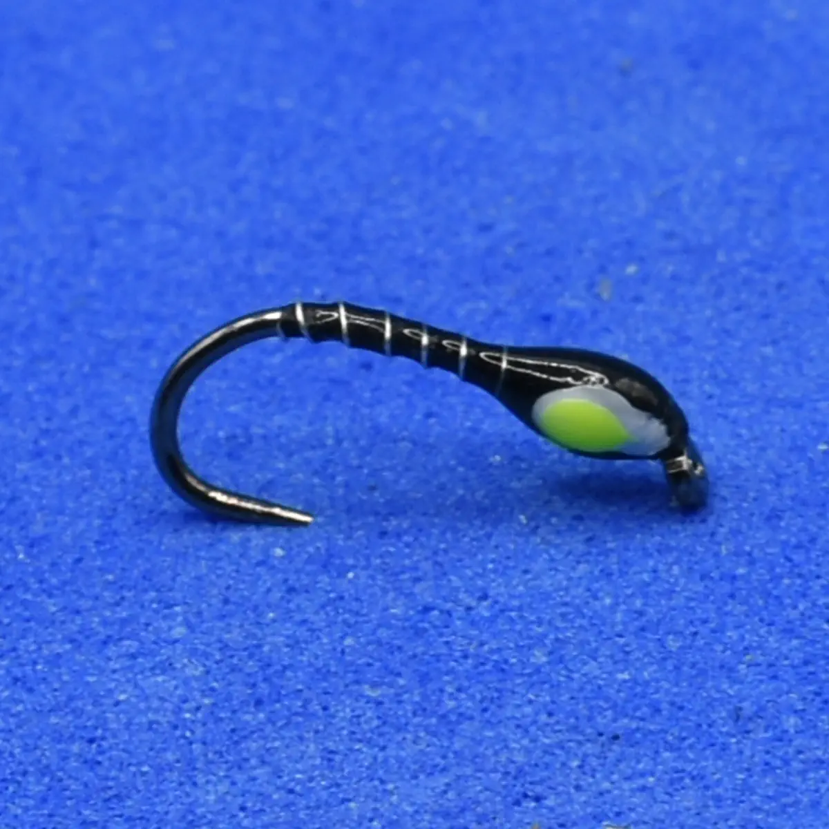 Black fishing jig head with a neon green and white bead, mounted on a curved hook against a blue background, used for lure fishing