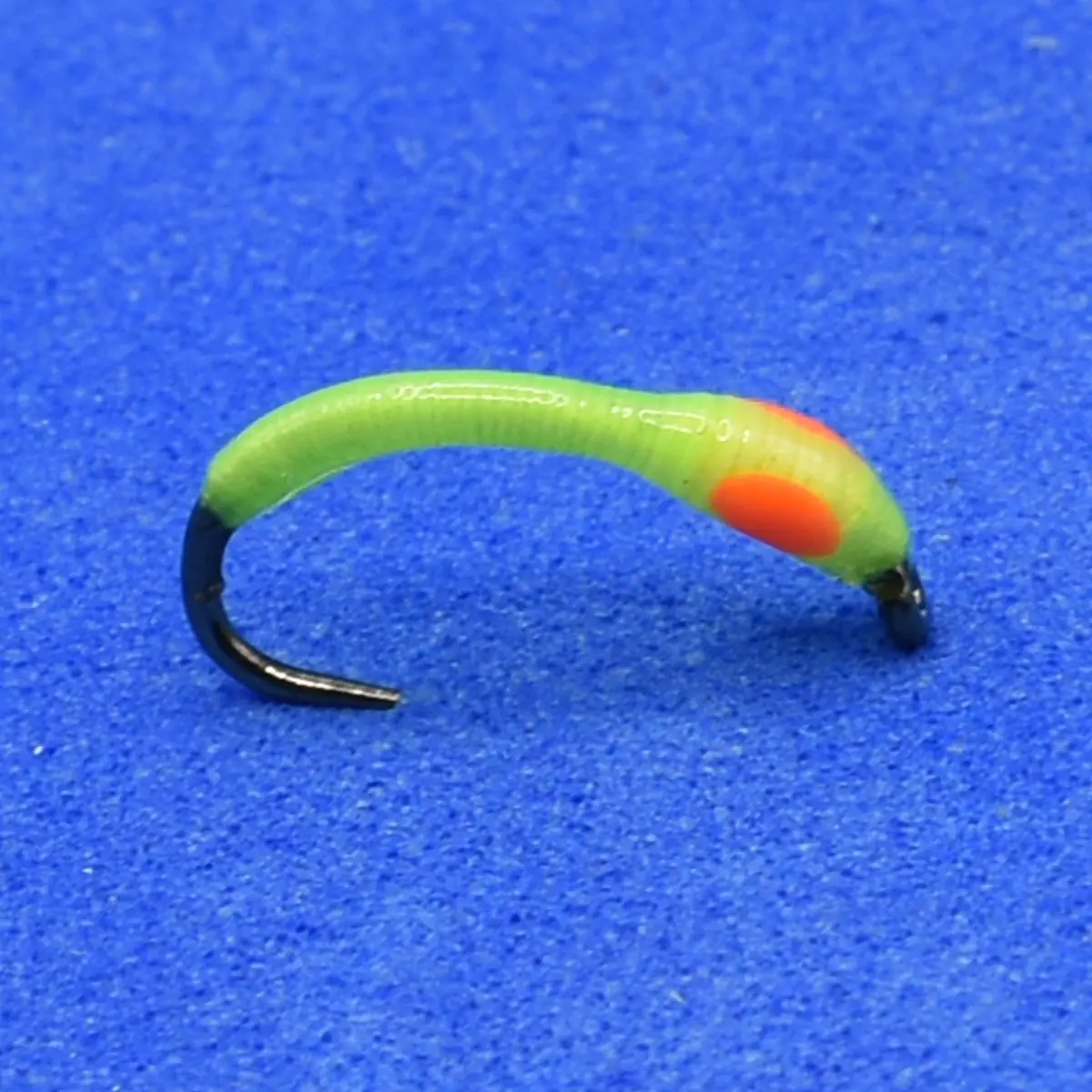 Green curved soft plastic fishing lure with an orange spot and a black hooked end on a blue background.