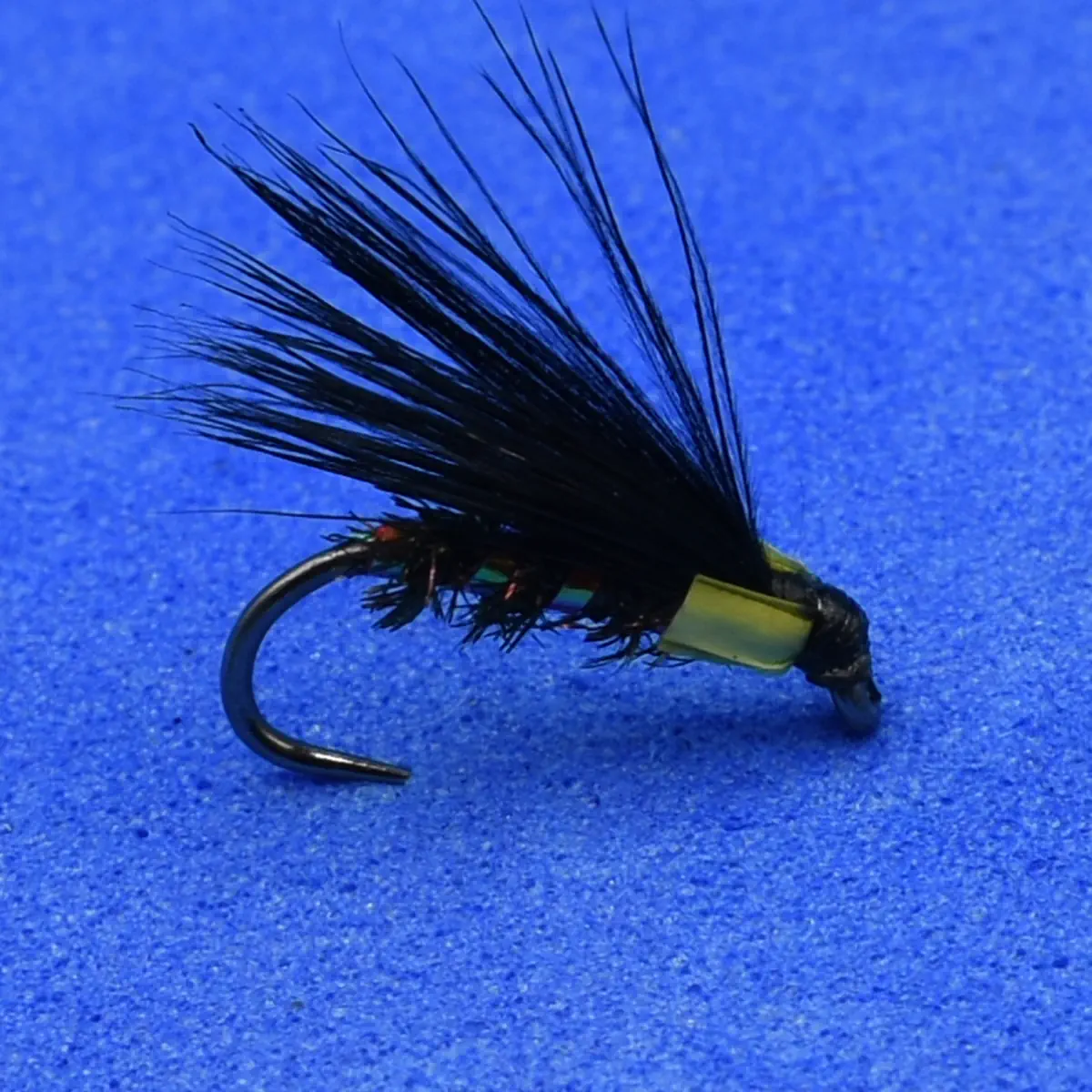 Black feathered fly fishing lure with a bead head on a curved hook, placed on a blue background.