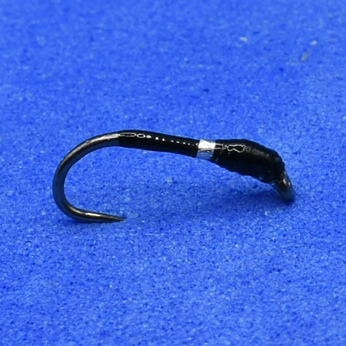 Small black fishing hook with a curved shape resting on blue fabric.