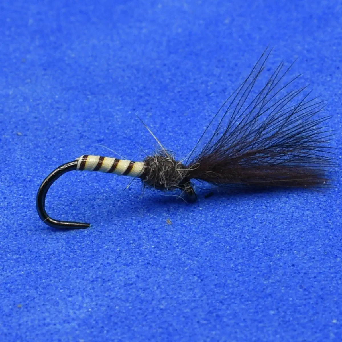 Fishing fly lure with striped body, dark hackle tail, and a curved hook on a blue background