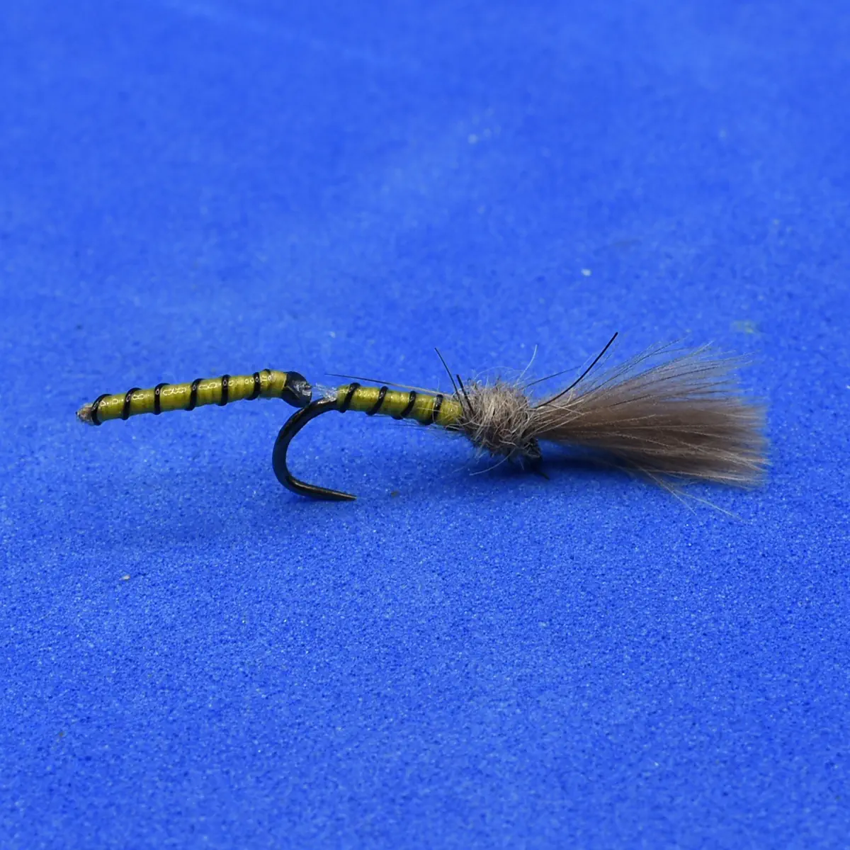 Bead-headed olive green fly fishing lure with fur tail resting on a blue background, hook visible.