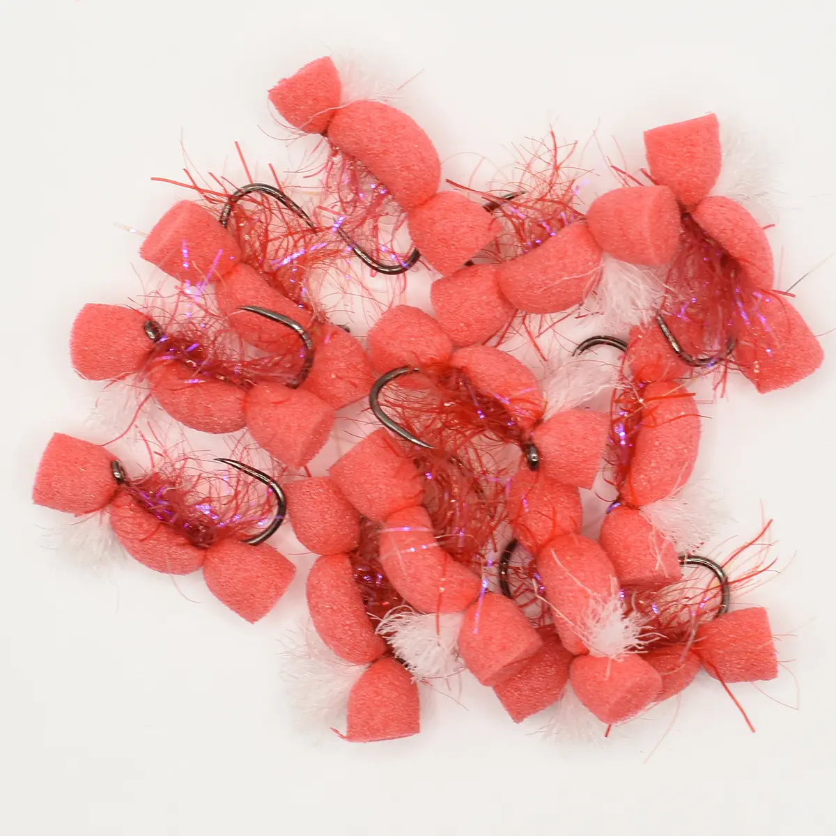 Pile of pink foam fishing lures with hooks and tinsel decoration on a white background.”,