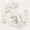 Close-up of small silver curved fishing hooks scattered on white fluffy cotton balls.