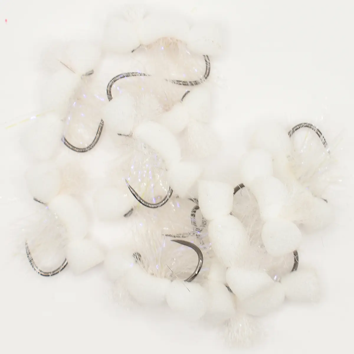 Close-up of small silver curved fishing hooks scattered on white fluffy cotton balls.