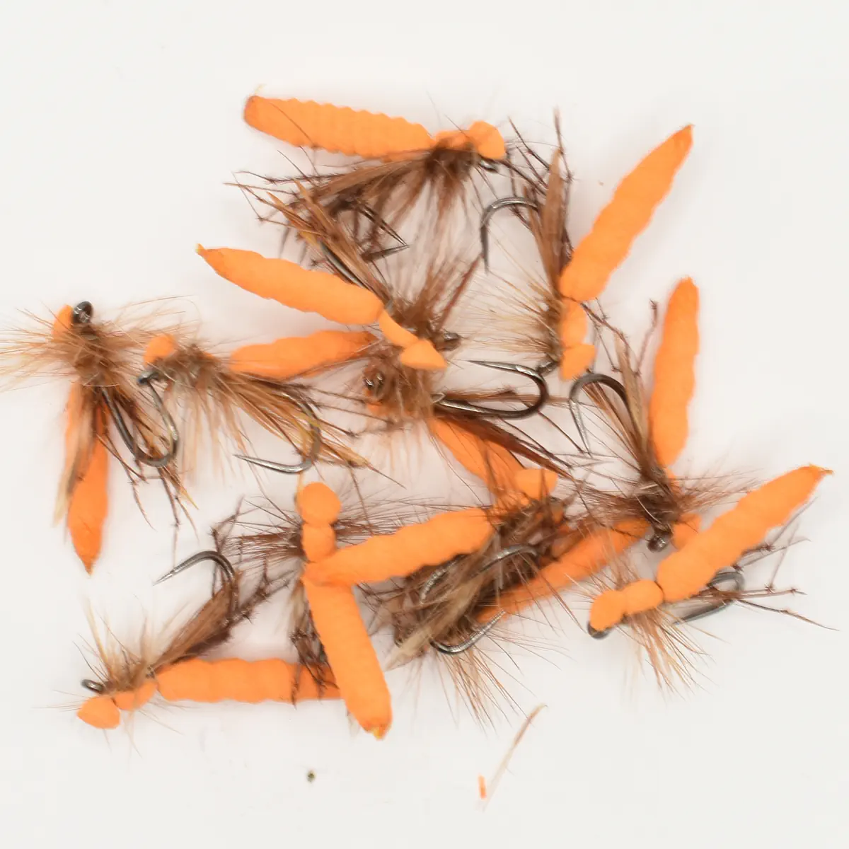 Assorted orange foam fishing flies with brown feather tails and sharp hooks on a white background, arranged in a cluster.