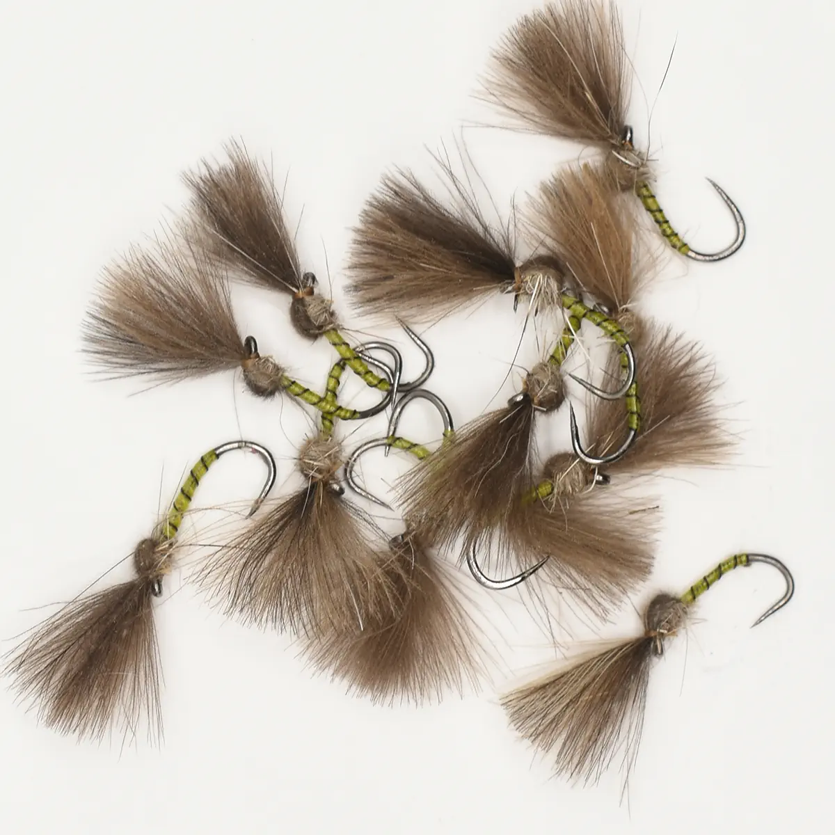 Collection of brown tufted fishing flies with olive-green bodies and sharp hooks, laid on a white background (fly fishing lures).