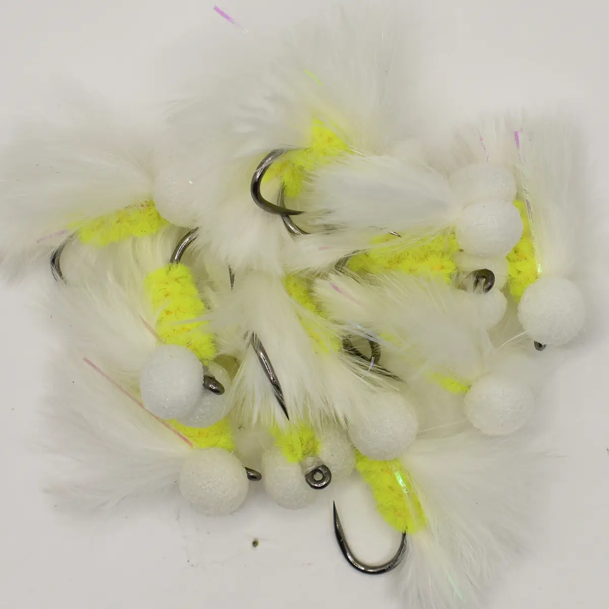 Assorted white feather fishing flies with neon yellow accents and small foam beads, hooks visible among the feathers.