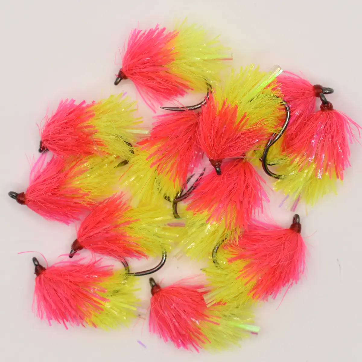 Assortment of neon pink and yellow fluffy fishing lures with metal hooks on a white background.