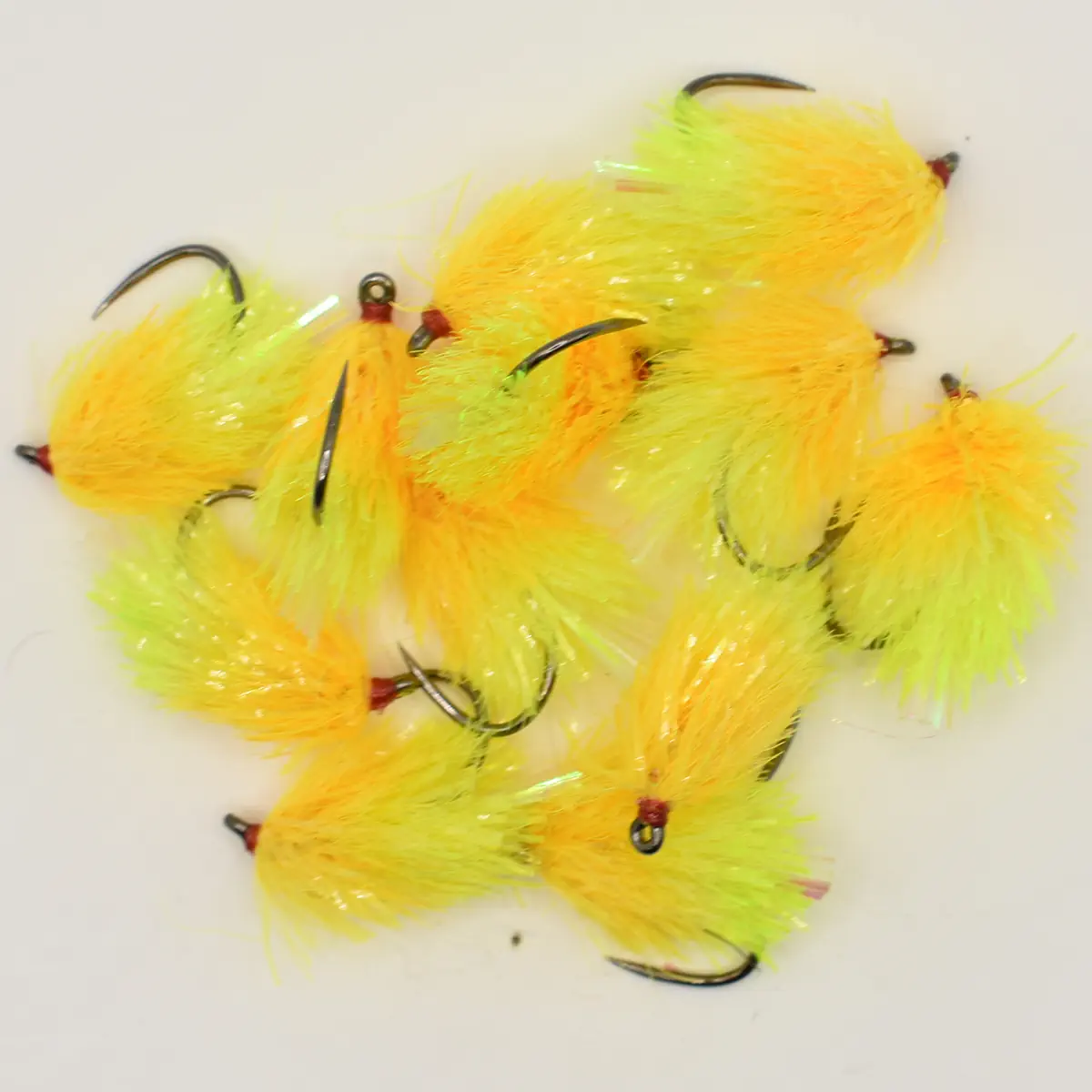 Pile of bright yellow and orange fluffy fishing flies with hooks on a white surface.