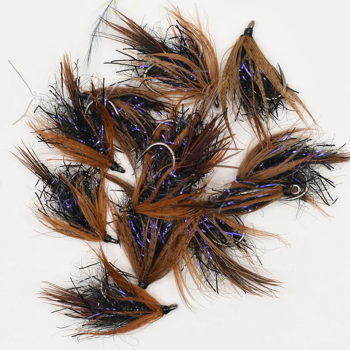 Assortment of brown and black fishing flies with purple tinsel and feather fibers on a white background