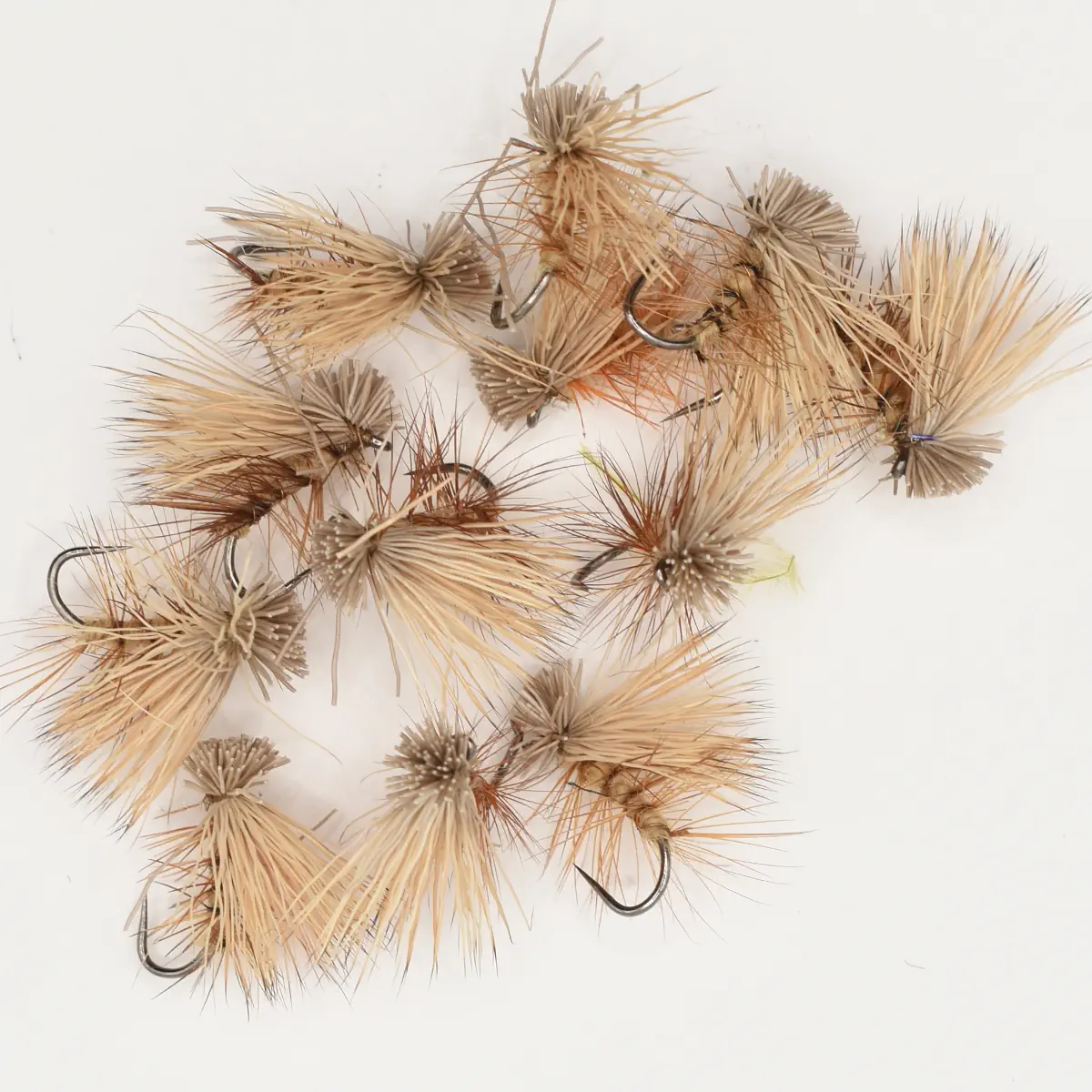 Assorted dry fishing flies with fluffy tan hackle tied on metal hooks on a white background, ready for casting.