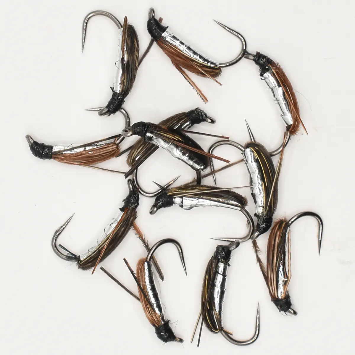 Collection of metallic fishing flies with feather tails arranged on a white background, ready for tying or use in fly fishing