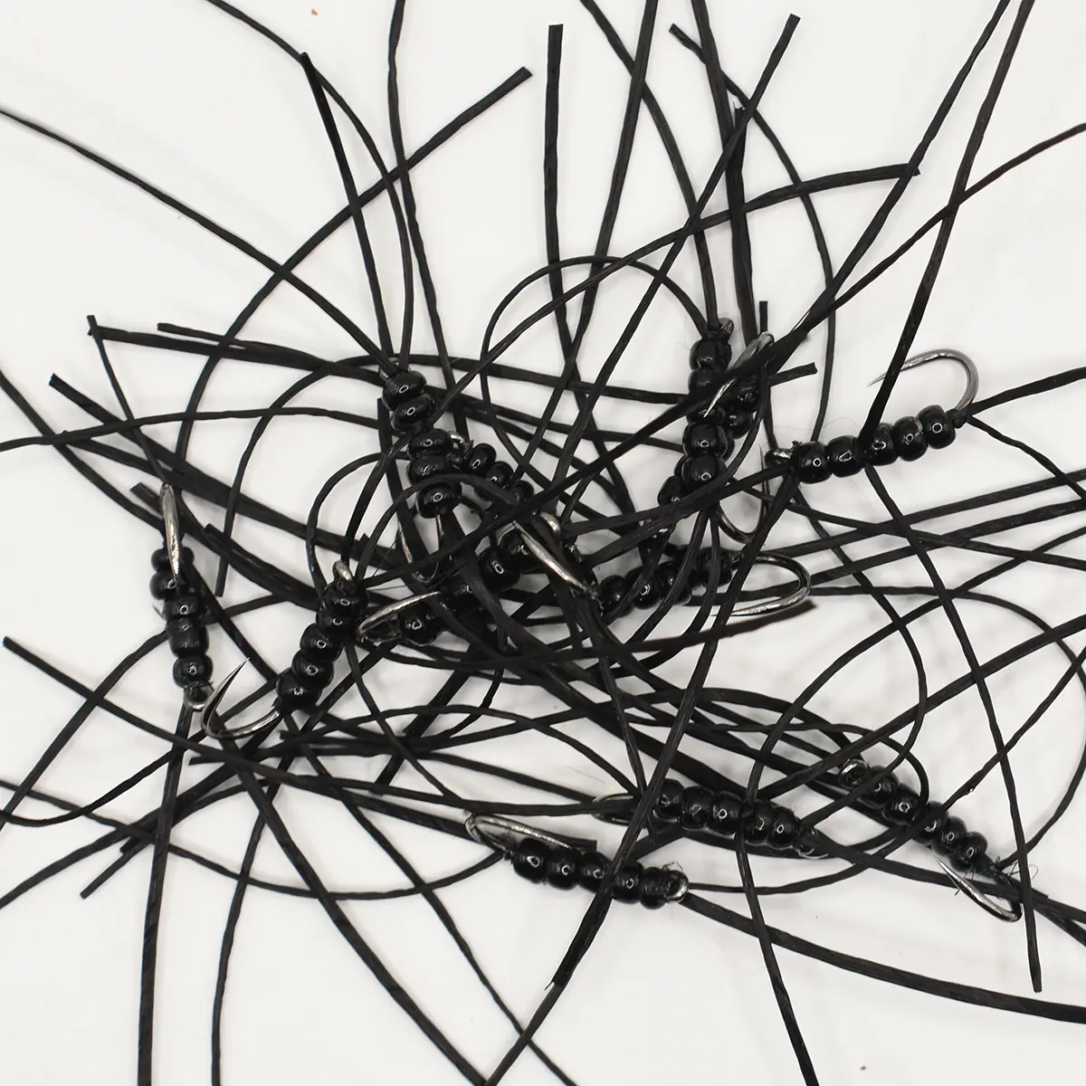 Mess of black leather cords with small black beads and metal clasps tangled on a white surface.