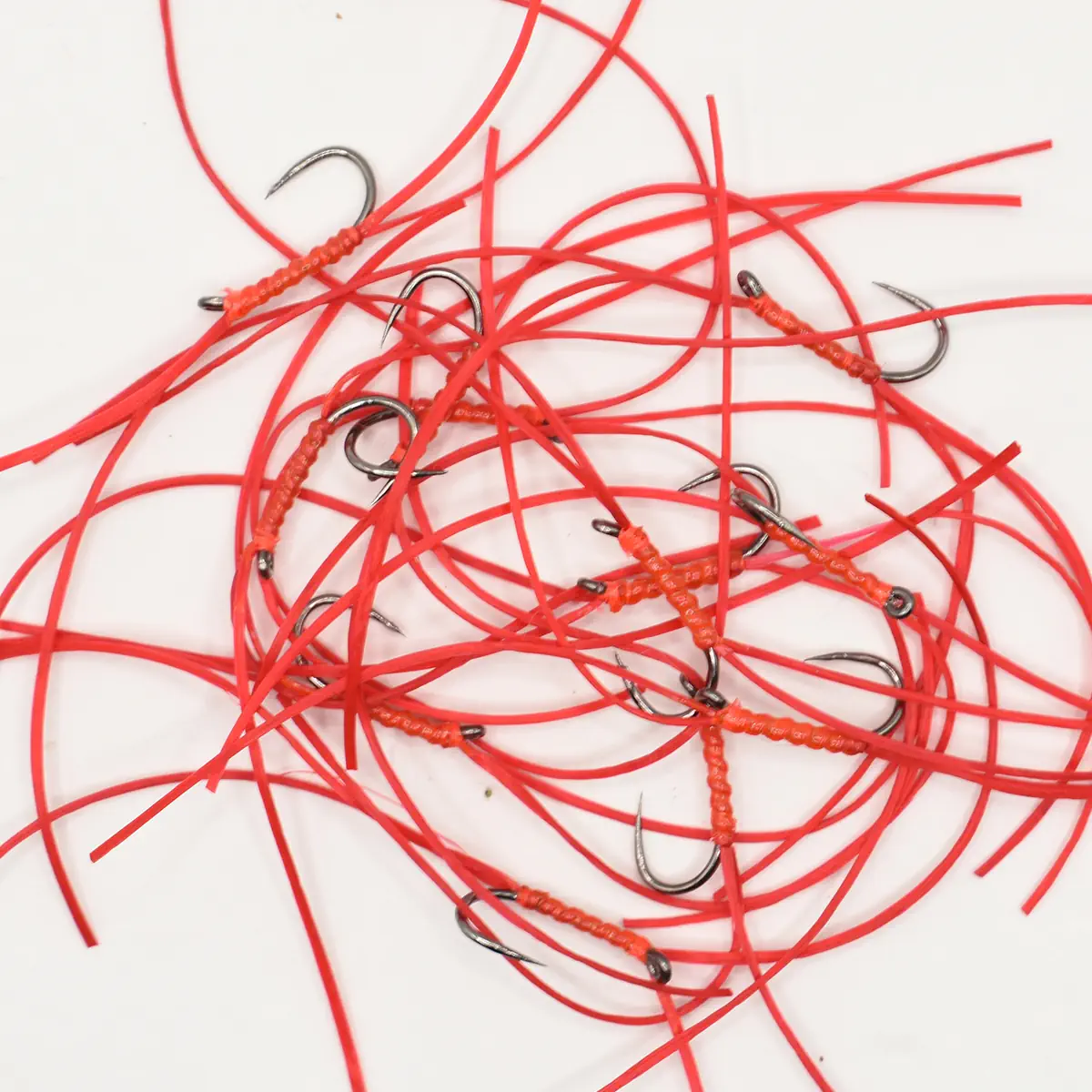 Pile of bright red fishing rigs with small curved hooks tangled together on a white surface, showing red tubing and wrapped sections