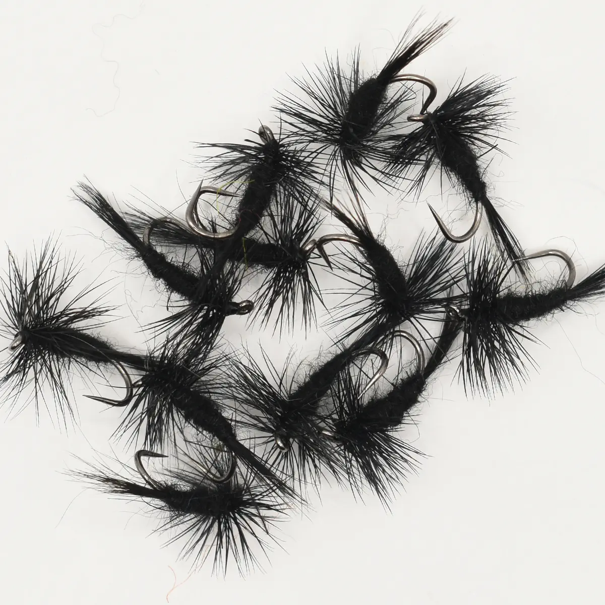 Several black fuzzy fishing flies with hooks arranged on a white background, used as lures for fly fishing
