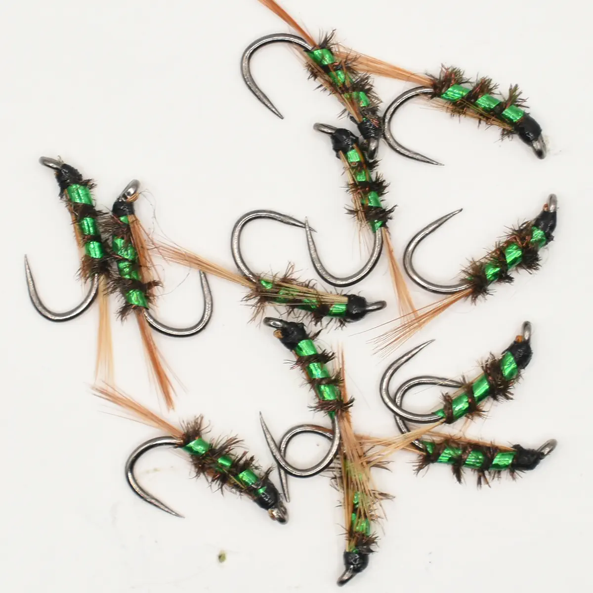Assortment of green-wrapped fishing flies with metallic hooks on a white background, used for fly fishing.