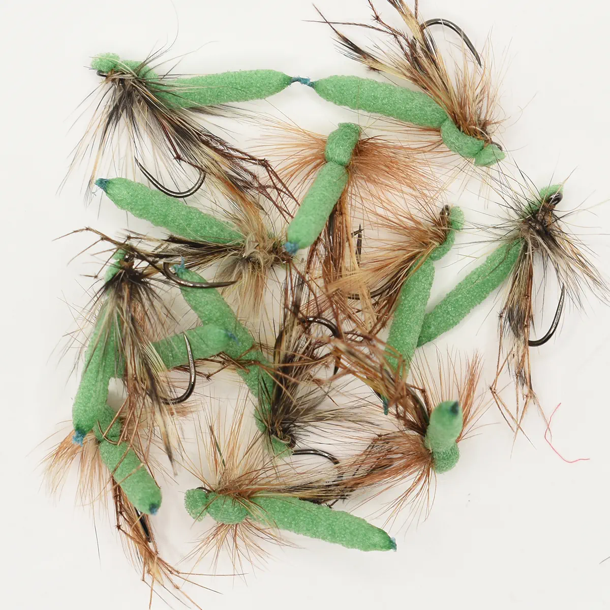 Assorted green foam-bodied fishing flies with brown hackle on hooks on a white background.