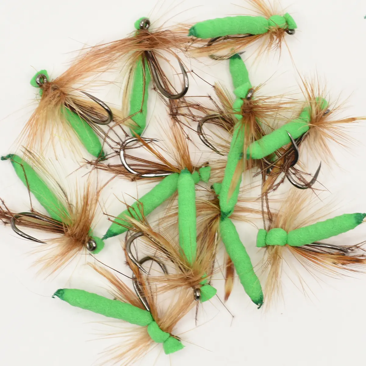 Assorted fly fishing lures with bright green foam bodies and brown feather skirts on a white surface.