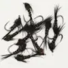 Assorted black fishing flies with tinsel and hair, scattered on a white surface for fly fishing.