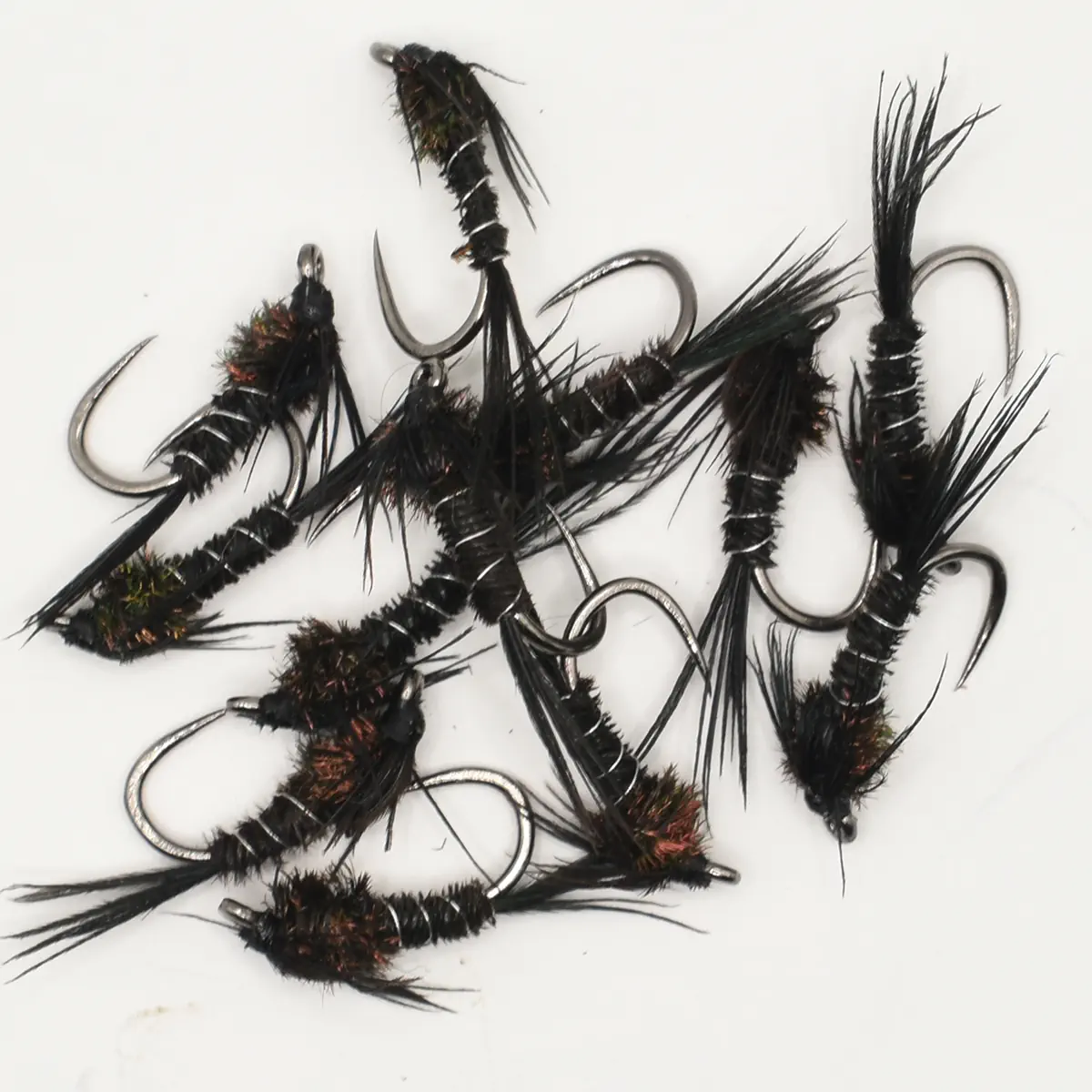 Assorted black fishing flies with tinsel and hair, scattered on a white surface for fly fishing.