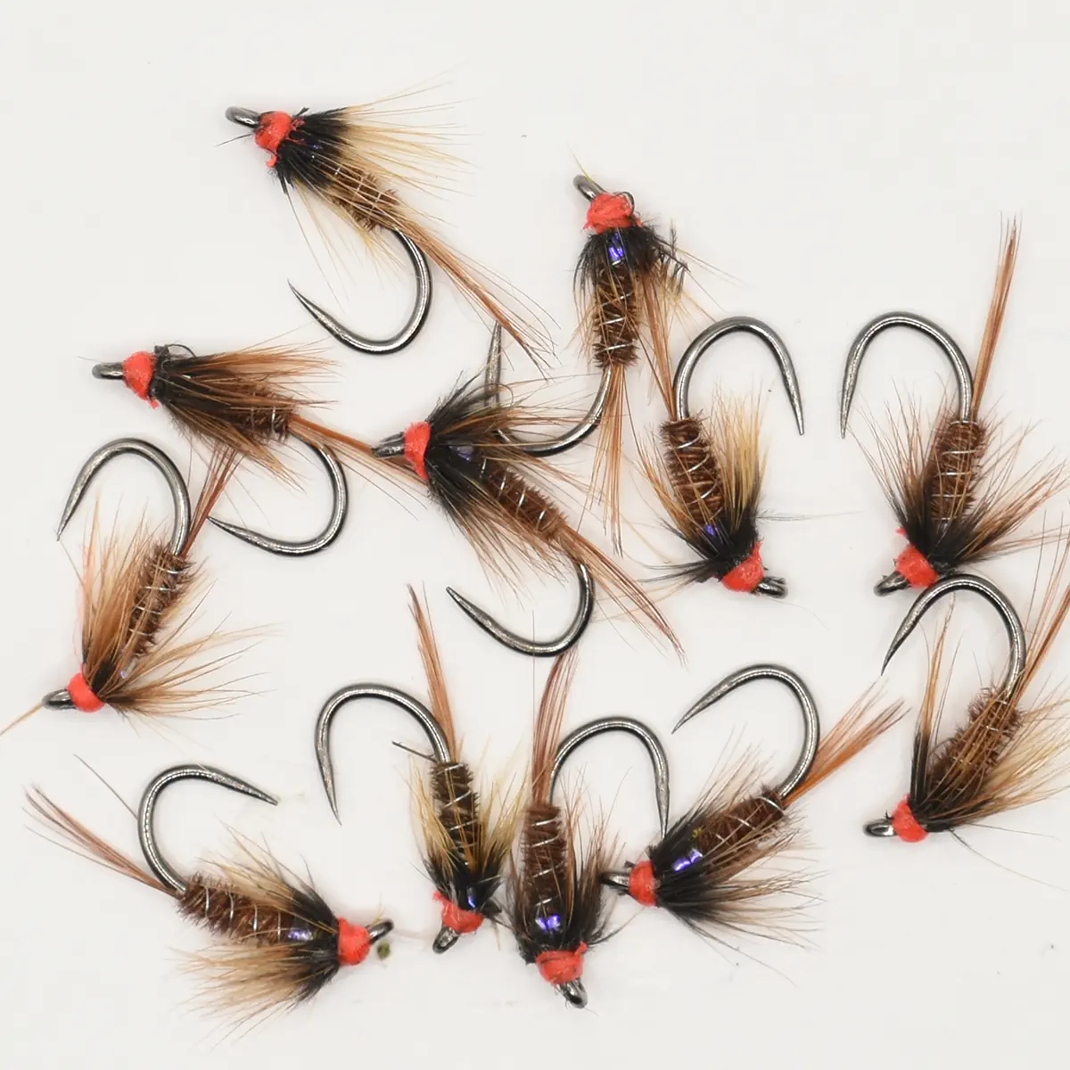 Assorted fishing flies with brown feather tails and orange-thread heads arranged on a white background.