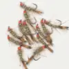 Collection of fishing flies with brown fur bodies, orange heads, and green bead accents laid on a white background (fly tying lures).