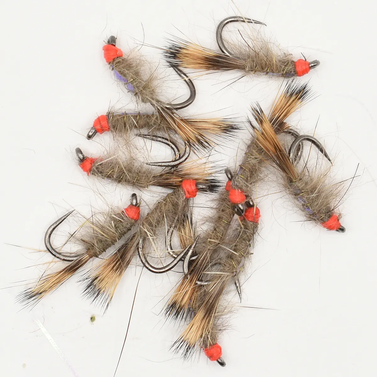 Collection of fur-covered fishing flies with orange thread heads and sharp metal hooks laid out on a white background