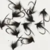 Collection of black feathered fishing flies with metal hooks scattered on a white background for fly fishing use