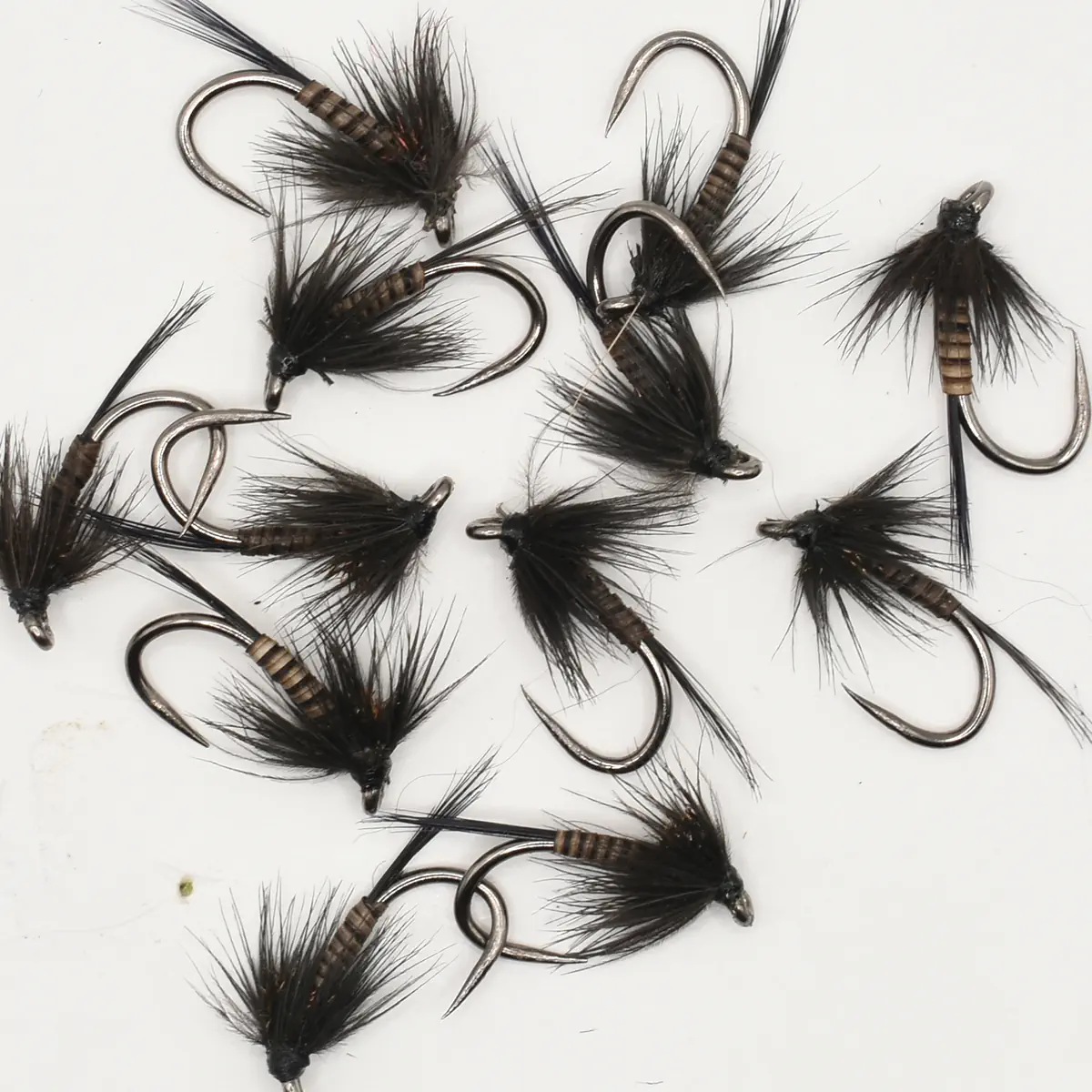 Collection of black feathered fishing flies with metal hooks scattered on a white background for fly fishing use