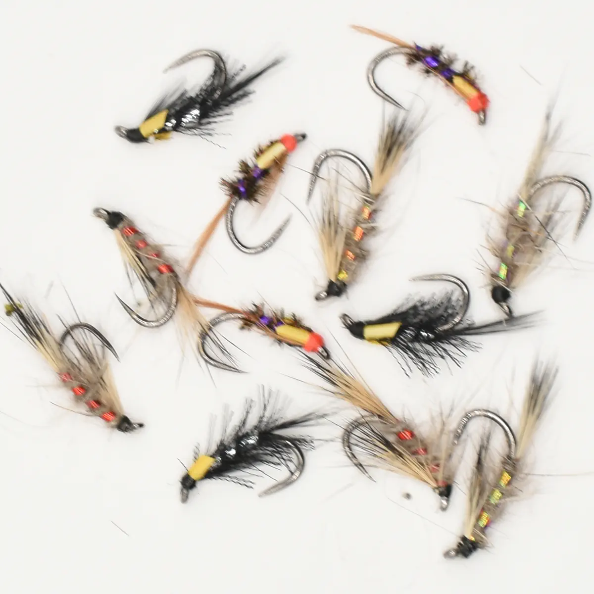 Assorted fly fishing lures with beads and feather tails scattered on a white surface