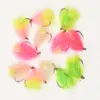 Assorted colorful fishing flies with bright pink, lime green, and peach feathers on metal hooks laid out on a white background