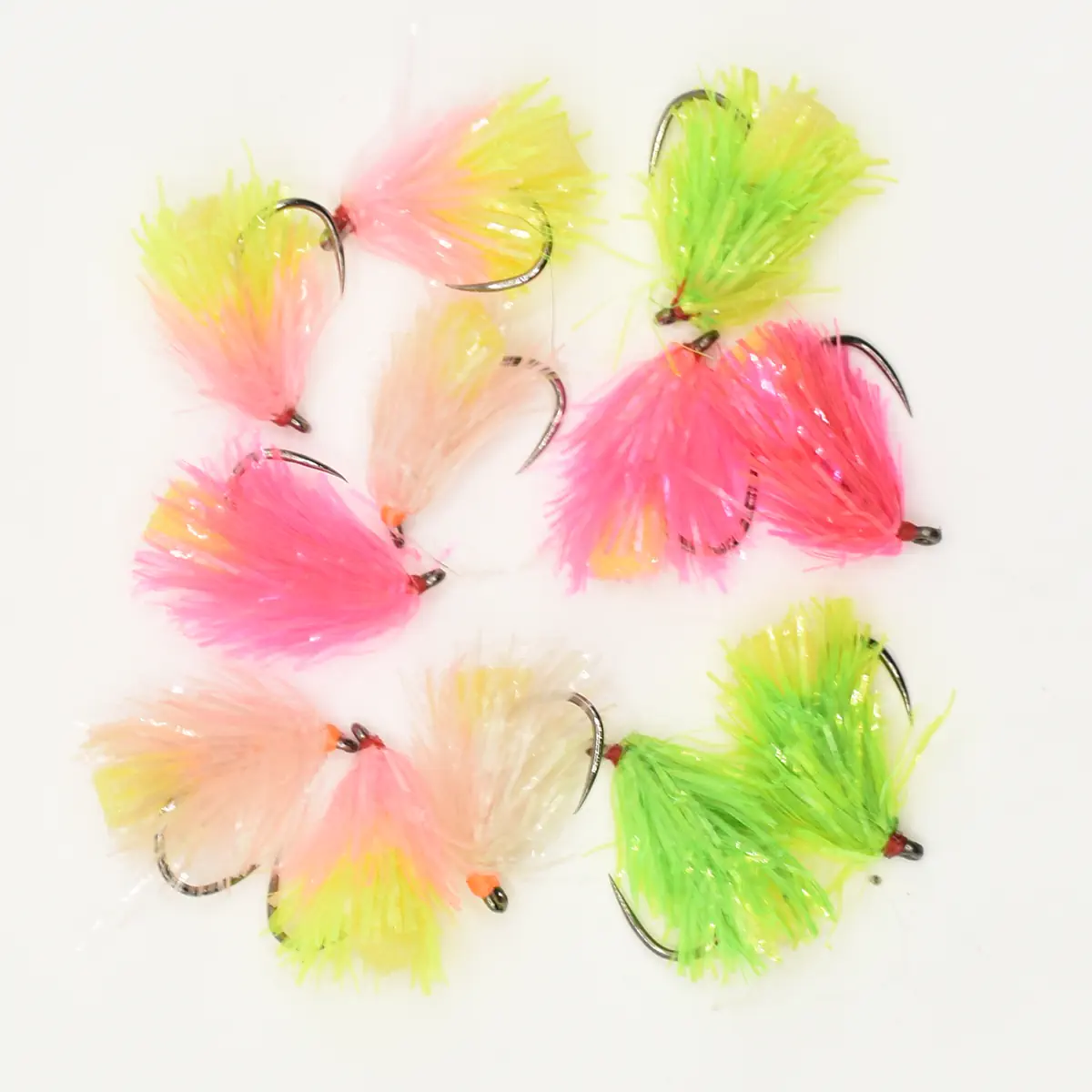 Assorted colorful fishing flies with bright pink, lime green, and peach feathers on metal hooks laid out on a white background