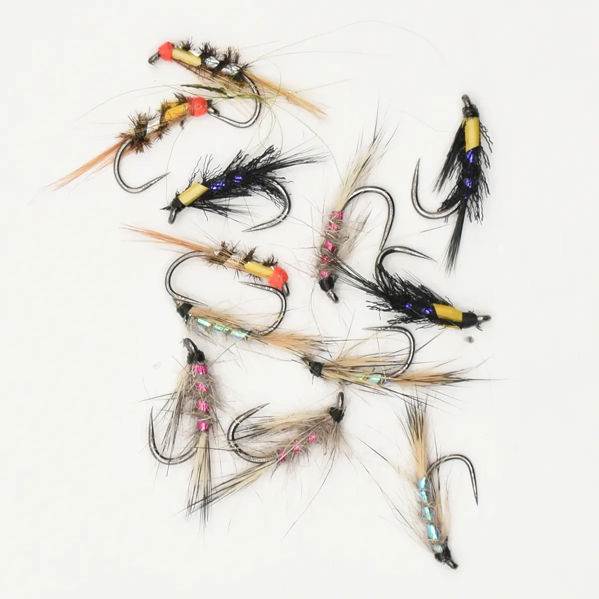 Assortment of artificial fishing flies with feathers and metallic tinsel laid on a white background.